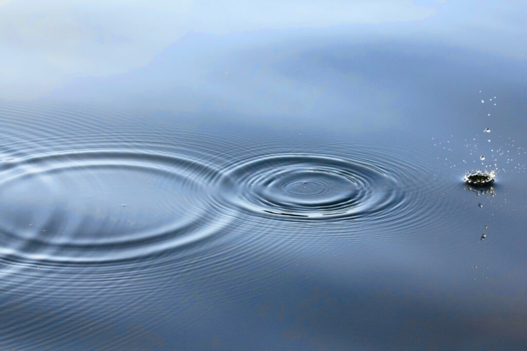 Three drops of rain in a pool of water causing ripples.