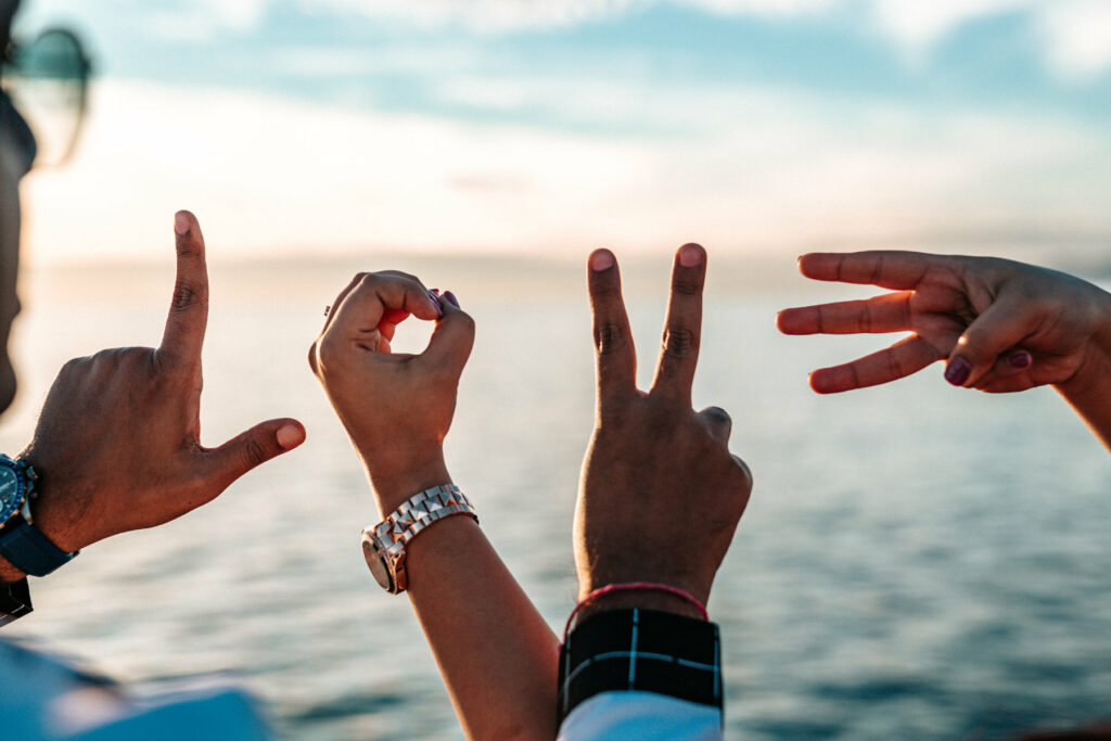 four hands spell out the word "love", an ocean in the background