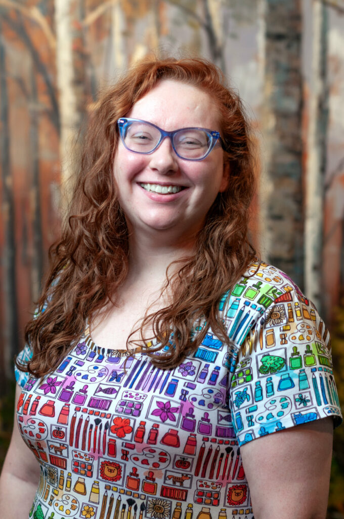 Becca McCormic has red hair, blue glasses, and a friendly smile.