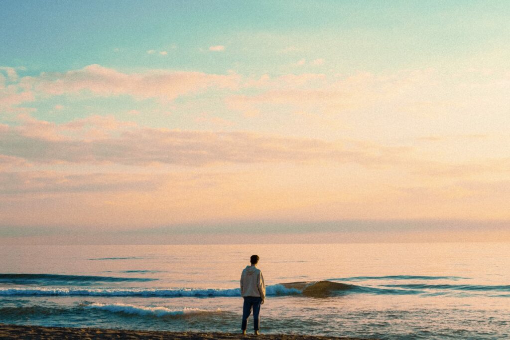 A person stands on a beach, reflecting on their personal journey.