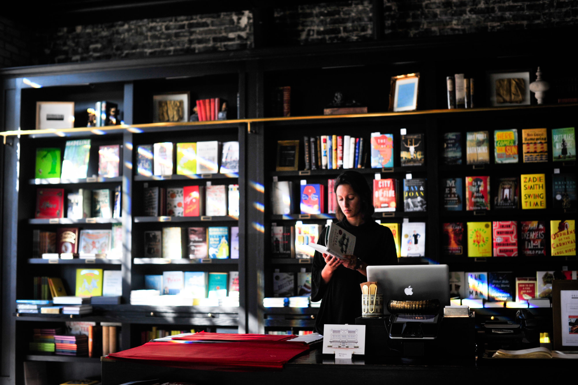 A person stands behind the counter of a bookshop reading.