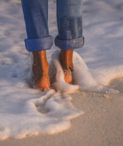 A person walks across a sandy beach, getting their feet wet.