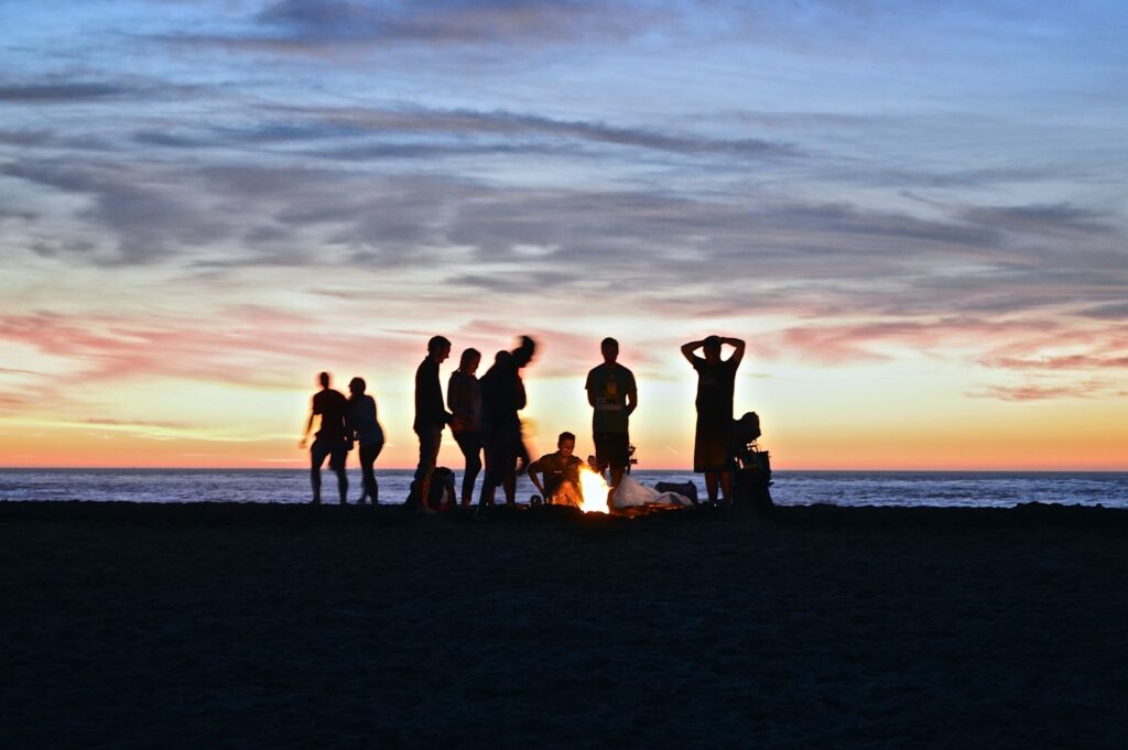 friends on a beach as dusk with a campfire