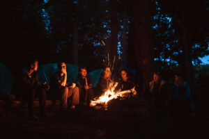 A group of people sit around a campfire at dusk